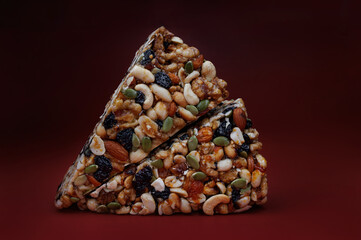 Two pieces of gozinak from various nuts with dried fruits on a red background.