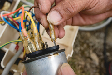 An electrician hook up wires to the terminals of a CBB65A-1 capacitor, part of a window type air conditioner control panel. - obrazy, fototapety, plakaty