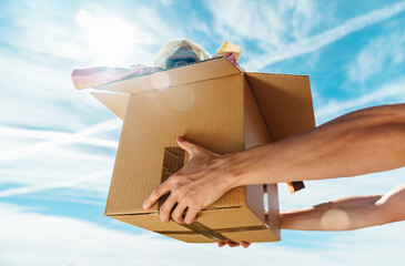 Hands holding cardboard box with clothes inside against sky. Concept donation and reuse or recycle...