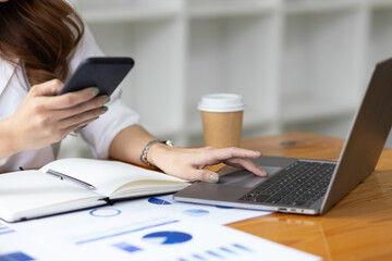 Attractive Asian businesswoman in office using smartphone writing work schedule in notepad.