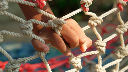 Close-up of children's hands, holding rope for climbing net on outdoor sports field.