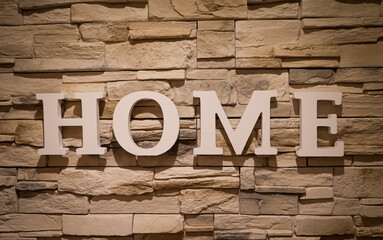An einer mit schmalen Steinen verkleideten Wand steht das Wort "Home".
