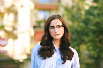 Outdoor portrait of pretty young woman with dark hair, wearing eyeglasses