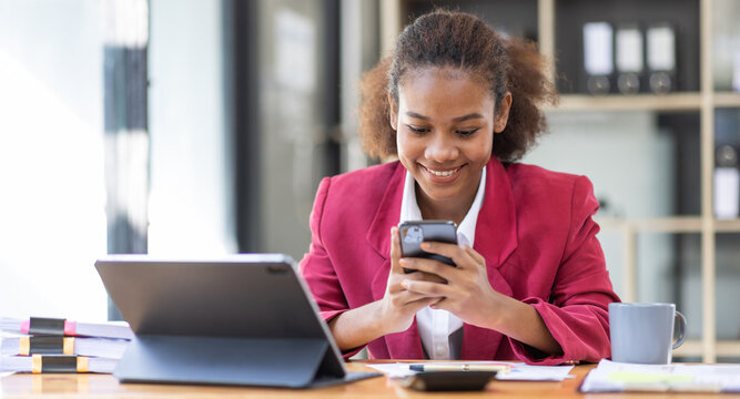 Positive beautiful young african black woman using mobile phone and  working on laptop in workplace, business investment Finance Entrepreneur concept.