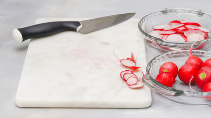 Fresh sliced radish close up on marble cutting board on light greybackground. Vegetable salad preparation process, recipe