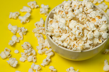 A plate full of popcorn on a yellow background. Delicious salty popcorn