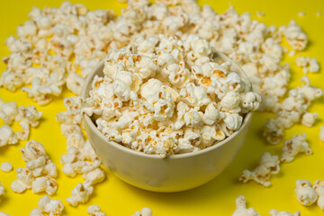 A plate full of popcorn on a yellow background. Delicious salty popcorn