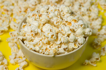 A plate full of popcorn on a yellow background. Delicious salty popcorn