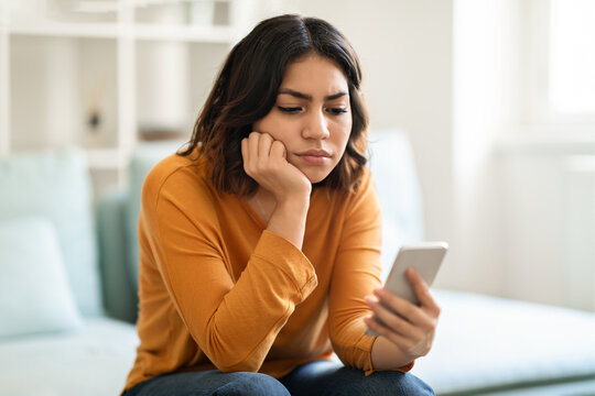 Pensive Upset Young Arab Woman Looking At Smartphone Screen At Home