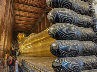 Wat Pho Temple in Bangkok, Thailand with huge lying golden Buddha statue, colorful ceiling and wall...