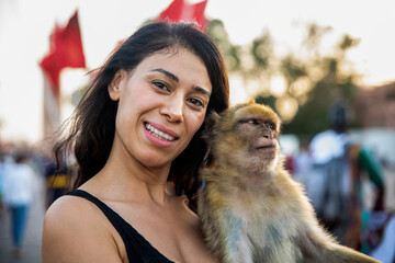 Young tourist enjoying a monkey in the Jemaa el Fna square in Marrakech next to the Moroccan flag,...