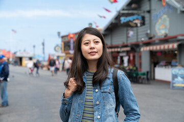Fototapeta premium portrait of smiling asian chinese woman tourist enjoying view while visiting Old Fishermanâs Wharf in California usa with colorful shop background