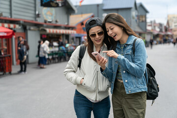 two happy asian Taiwanese girls looking at information on phone and discussing which local seafood restaurant to try on the street at Old Fishermanâs Wharf in usa