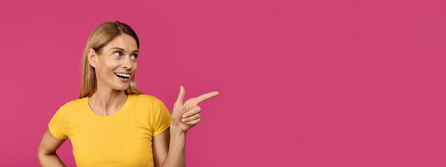 Smiling adult european woman with open mouth pointing finger at empty space