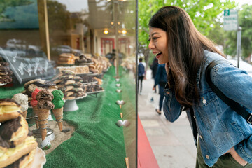 side view of excited asian chinese girl looking at ice cream cones in the window outside a bakery...