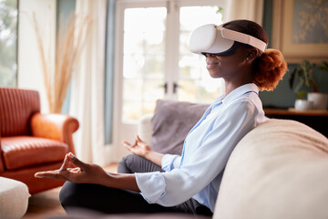 Woman Meditating On Sofa At Home Wearing VR Headset And Interacting With AR Technology