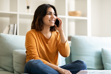 Obraz premium Young Arab Woman Talking On Cellphone And Relaxing On Couch At Home