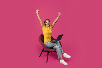 Satisfied adult european woman sitting on chair with laptop, raising hands, celebrating success and...