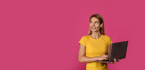 Smiling mature european female with laptop looking at empty space, isolated on purple background