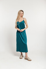 Fashion pretty stylish happy smiling woman model with blonde hairstyle in vintage long Turquoise dress with shoes stands on a white background in studio