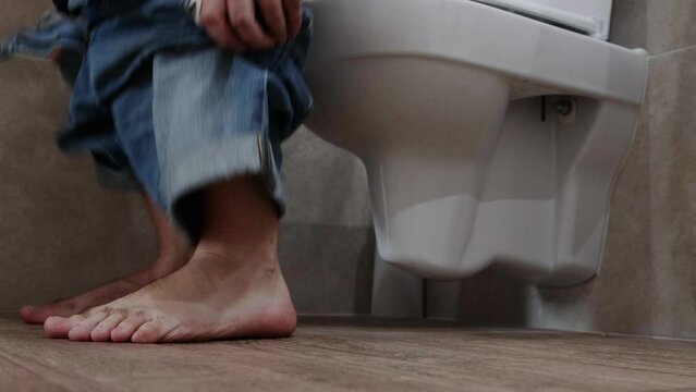 A man goes to the toilet in the toilet, takes off his denim shorts and begins the process of defecation. Healthy digestive tract and intestines.