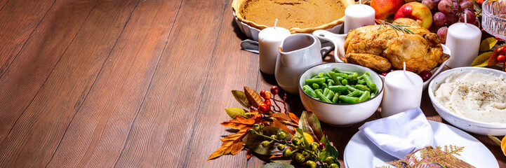 Thanksgiving family party dinner table setting with plates, cutlery, glasses, traditional dishes - baked turkey or chicken, pumpkin pie, fruits, mashed potatoes, green beans, wooden background