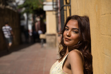 Young and beautiful woman with long brown hair and cinnamon skin leaning on a brick bench with a yellow wall in the background, with a sensual look. Concept of beauty, sensuality.