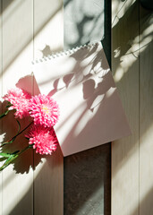 Shadows of plants fall on an open empty notebook. Nearby are red flowers on a white wooden background. Floral concept of keeping a diary, making lists, taking notes. Copy space.