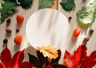 A round paper frame is found along with yellow, red, green fallen leaves, physalis flowers and fir cones on a white wooden background. Autumn, fall, thanksgiving day concept. Flat lay. Copy space.