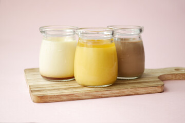  Caramel, chocolate and mango pudding in a glass jar on pink background 