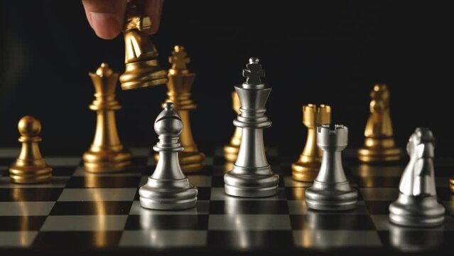 Hands are picking up gold and silver chess on a game board that uses the concept of planning for victory.