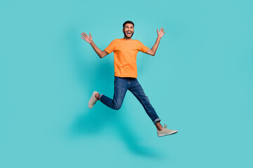 Fototapeta na wymiar Full length photo of funny excited guy wear orange t-shirt jumping high smiling isolated teal color background
