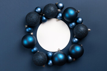 White empty circle with frame of blue matte and glitter Christmas balls on dark blue background with copy space