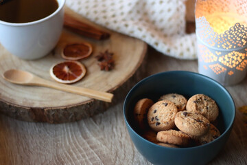 Cup of tea or coffee, seasonal spices, bowl of cookies, blanket, pumpkins, colorful leaves, books and candle. Cozy autumnal atmosphere at home. Selective focus.