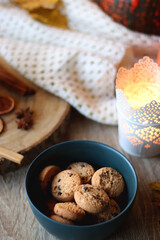 Cup of tea or coffee, seasonal spices, bowl of cookies, blanket, pumpkins, colorful leaves, books and candle. Cozy autumnal atmosphere at home. Selective focus.