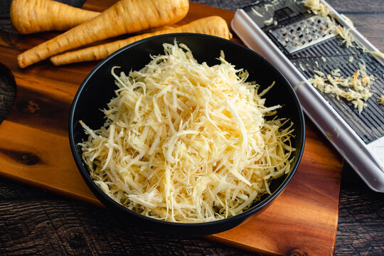 Bowl of Shredded Parsnips on a Wood Cutting Board: Whole and shredded parsnips with a mandoline