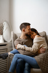 Obraz premium Romantic couple at home. An Attractive young woman and handsome man are enjoying spending time together while siting coddling on the armchair