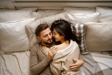 Naklejka na ściany i meble Beautiful young happy couple relaxing in bed and smiling, embracing