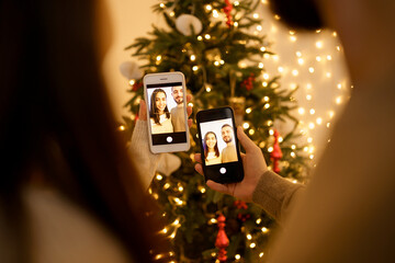 Fototapeta na wymiar Woman and man making photo with smartphone on beautiful fir tree background, full of lights. Social media holidays, back view.