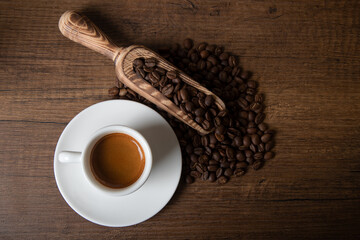 White cup of espresso with coffee beans on wooden background
