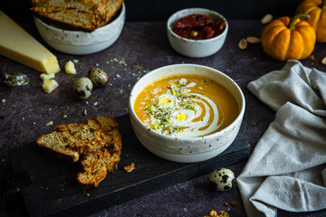 Homemade pumpkin cream soup with quail eggs, parmesan , sour cream and pistachios and biscotti with dried tomatoes and pistachios on dark background .