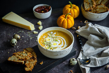 Homemade pumpkin cream soup with quail eggs, parmesan , sour cream and pistachios and biscotti with dried tomatoes and pistachios on dark background .