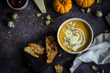 Homemade pumpkin cream soup with quail eggs, parmesan , sour cream and pistachios and biscotti with dried tomatoes and pistachios on dark background .