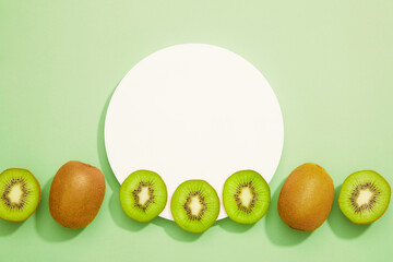 Kiwi fruit in a horizontal row with slices underneath a white podium circle of stage on a light green background.
