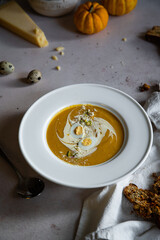 Homemade pumpkin cream soup with quail eggs, parmesan , sour cream and pistachios and biscotti with dried tomatoes and pistachios on white background 