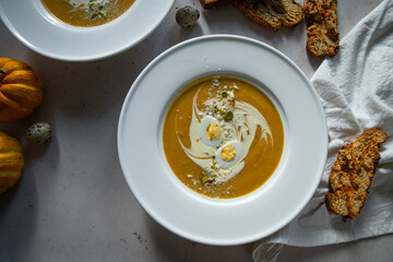 Homemade pumpkin cream soup with quail eggs, parmesan , sour cream and pistachios and biscotti with dried tomatoes and pistachios on white background 