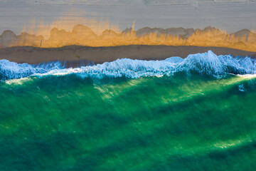 Obraz na płótnie Canvas Wave breakers during sunset shot directly from above, with the top of the wave illuminated by the sun.