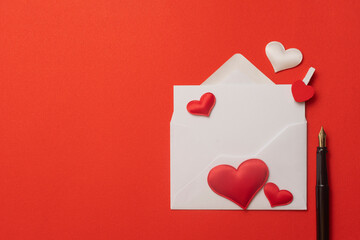 Valentine's day concept: blank envelope on red background sorrounded by hearts and a fountain pen
