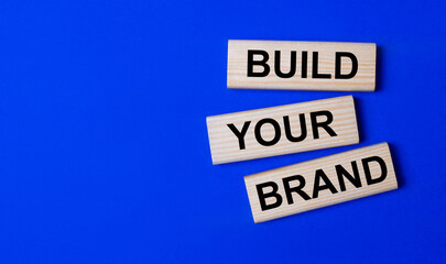 Three wooden blocks with the text BUILD YOUR BRAND on a bright blue background. Copy space