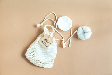Cotton reusable make-up remover pads in a fabric bag, and a ball of cotton on a beige background.